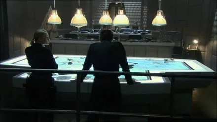 Two figures silhouetted at a large illuminated map table in a darkened war room.