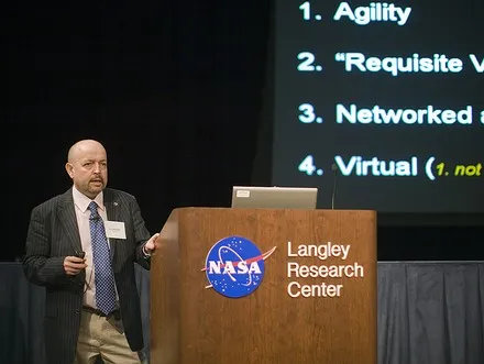 Ken Thompson speaking at a lectern branded NASA Langley Research Center, beside a screen listing agility, requisite variety, networked and virtual.