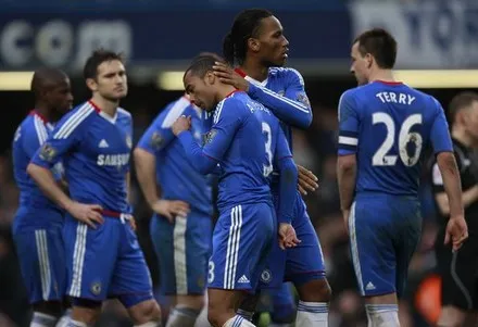 Chelsea footballers standing together on the pitch, one with a hand raised to his head.